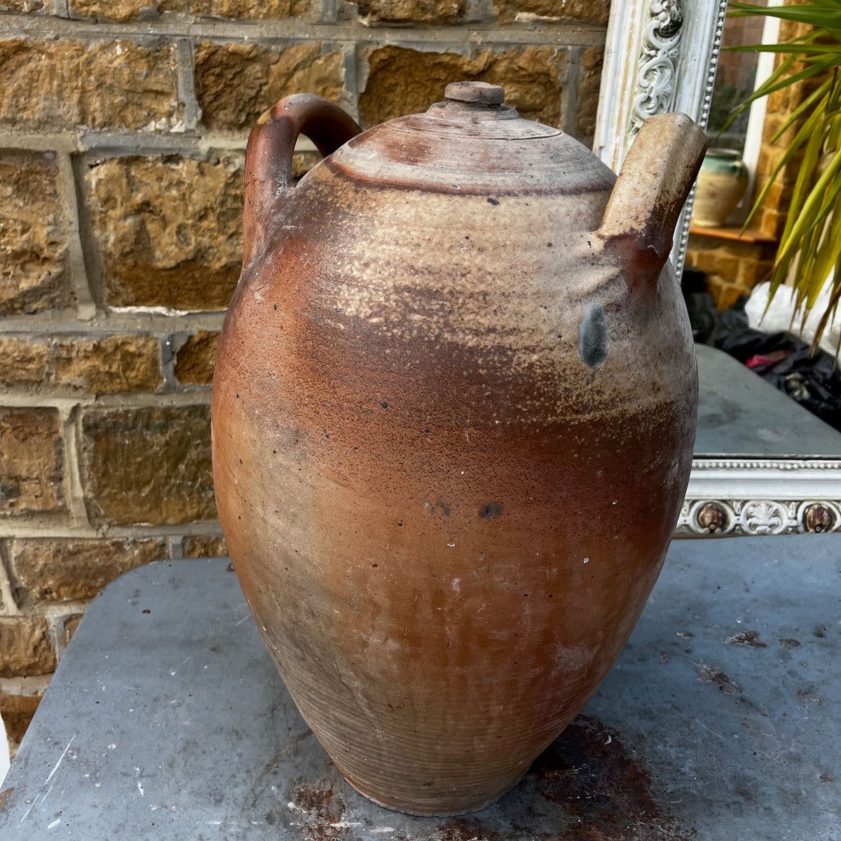 A large handmade ceramic amphora-style vase with a lid, featuring a rustic earthy brown and beige glaze