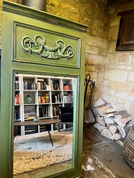 A trumeau-style mirror with a rectangular frame painted in Constance Moss green, accented with distressed gold detailing. The weathered finish highlights ornate carvings at the top, giving it an aged, elegant appearance