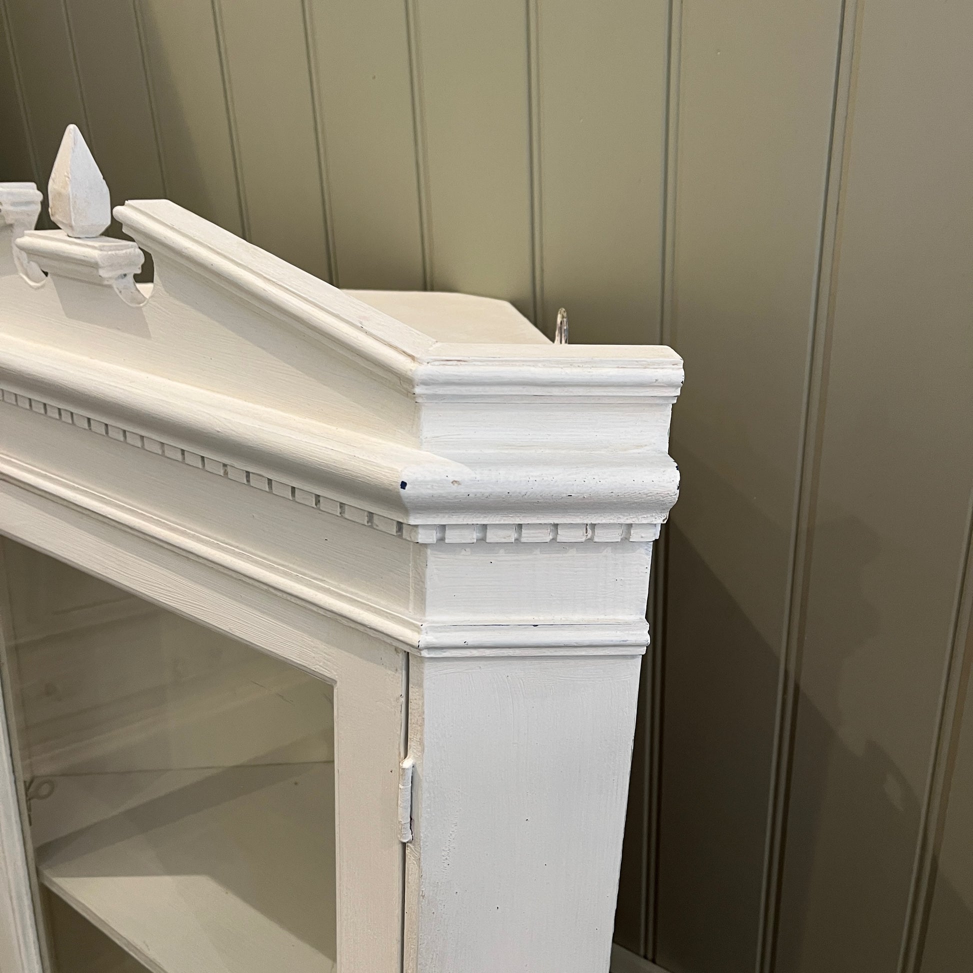A white wooden corner cabinet designed for bathroom use, which fits into a corner, with a single door and interior shelves for practical storage, offering a clean and classic look.