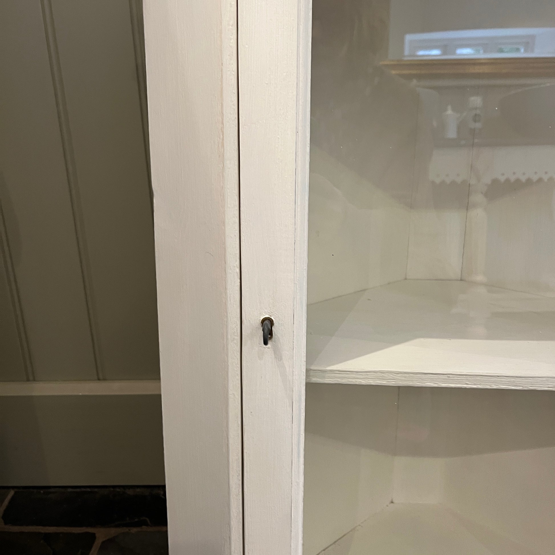 A white wooden corner cabinet designed for bathroom use, which fits into a corner, with a single door and interior shelves for practical storage, offering a clean and classic look.