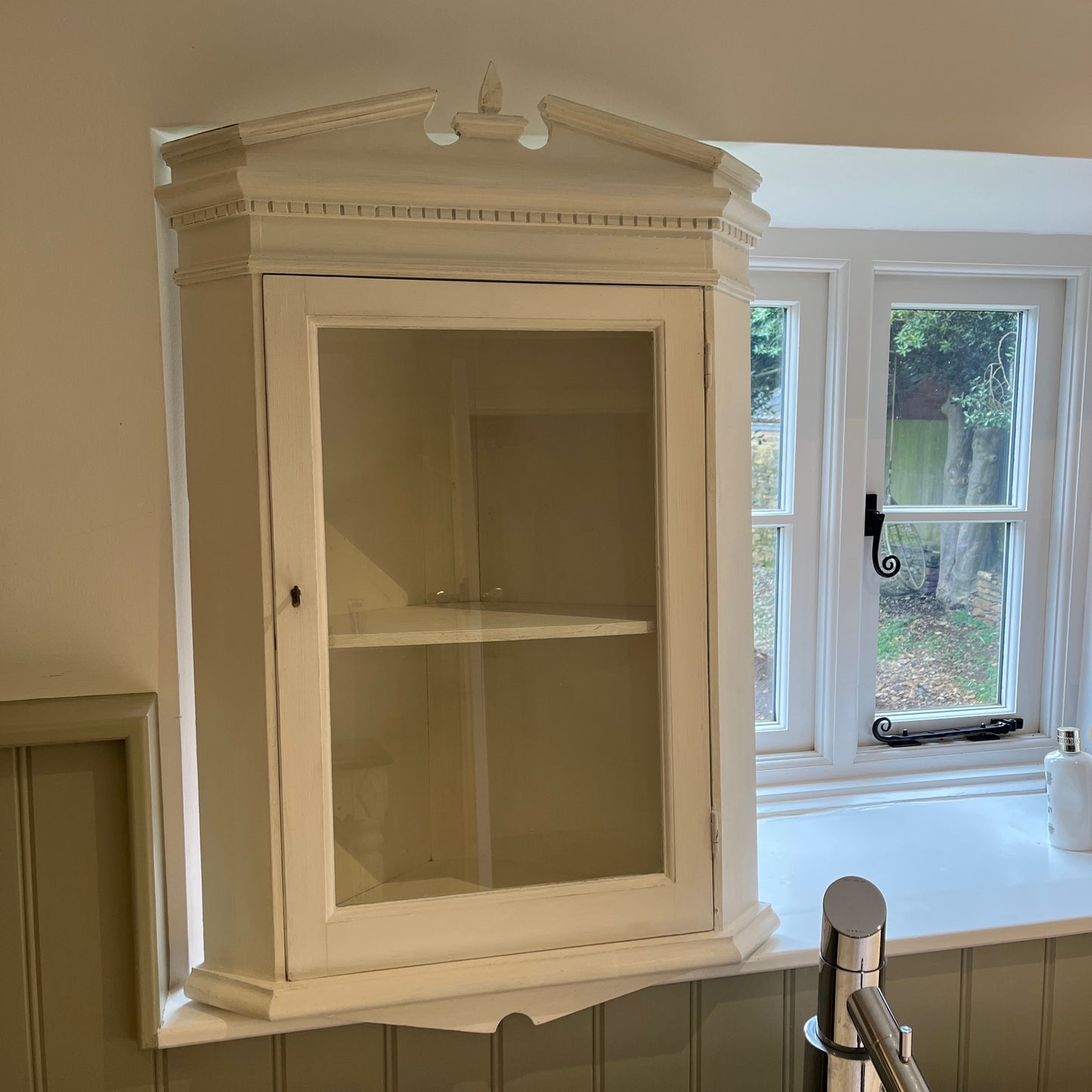 A white wooden corner cabinet designed for bathroom use, which fits into a corner, with a single door and interior shelves for practical storage, offering a clean and classic look.